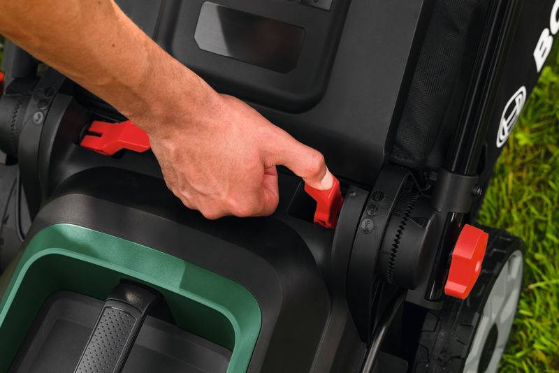 „Eine Person stellt einen roten Hebel an einer schwarzen Maschine ein, die wie Gartengeräte aussieht, mit Rädern im Gras im Hintergrund.