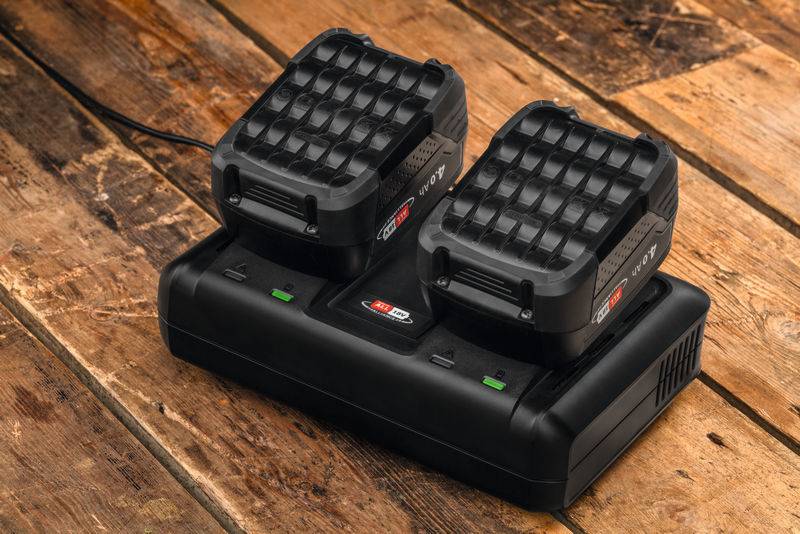 „Ein Dual-Port-Batterieladegerät mit zwei Batterien, platziert auf einer Holzoberfläche. Das Ladegerät hat LED-Anzeigen, die den Ladestatus anzeigen.