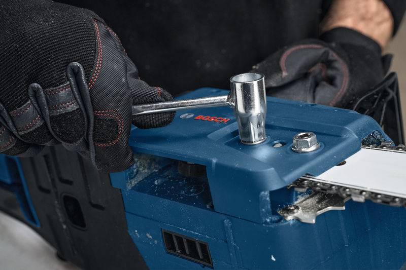 Eine Person mit Handschuhen benutzt einen Schraubenschlüssel, um einen Bolzen an einer Kettensäge zu befestigen, wobei sie sich auf eine Wartungs- oder Montageaufgabe konzentriert.