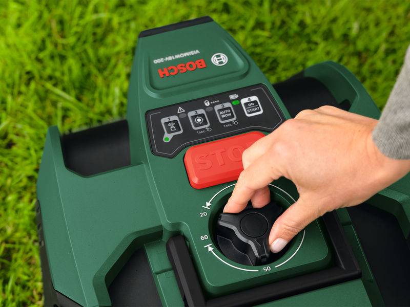 Eine Hand stellt ein Schieberregler auf einem grünen Rasenmäher mit Bosch-Logo ein, umgeben von frischem grünem Gras, was den Fokus auf einfache Bedienung unterstreicht.