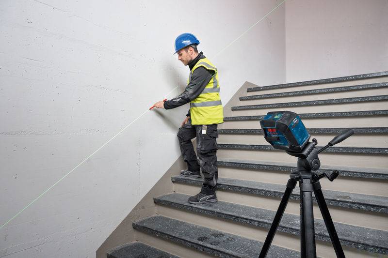 Ein Bauarbeiter in einem Schutzhelm und einer Warnweste verwendet ein Laserniveau auf einer Treppe, um die Genauigkeit während der Installation zu gewährleisten.