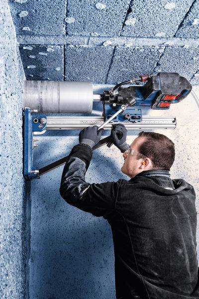 Eine Person benutzt ein Elektrowerkzeug, um in eine blaue, geflieste Wand zu bohren, trägt Schutzbrille und Handschuhe und konzentriert sich auf Bauarbeiten.
