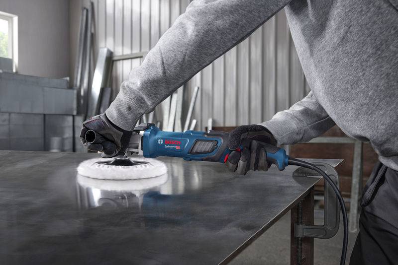 Eine Person, die Handschuhe trägt, verwendet einen Bosch-Poliermaschine auf einer Metalloberfläche in einer industriellen Umgebung, was die Verwendung eines Werkzeugs zum Oberflächenfinish veranschaulicht.