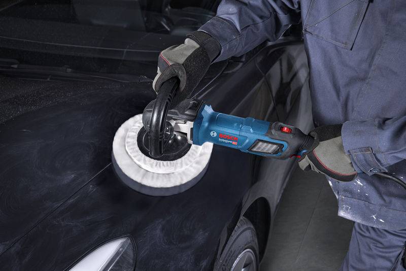 Person, die eine Motorhaube eines Autos mit einem elektrischen Polierer poliert, trägt Schutzhandschuhe und einen blauen Arbeitsanzug.
