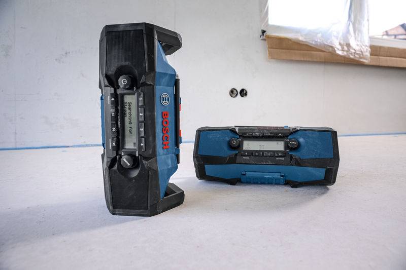 Zwei blau-schwarze tragbare Bosch-Radios auf einer Baustelle. Eines steht aufrecht; das andere liegt auf dem Rücken. Baustelle im Umbau.