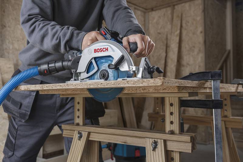 Person, die eine Bosch-Elektrokettensäge verwendet, um Holz auf einem Sägebock in einer Werkstattumgebung zu schneiden.