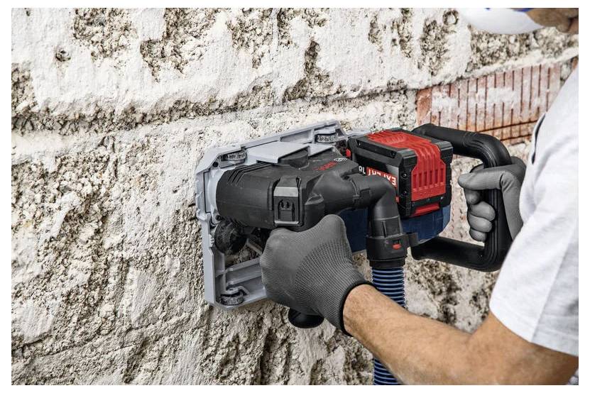 Arbeiter, der eine Wandschneidesäge verwendet, um eine Nut in eine Beton- oder Steinwand zu schneiden, hält das Werkzeug mit behandschuhten Händen, während sich Staub um den Schnitt ansammelt.