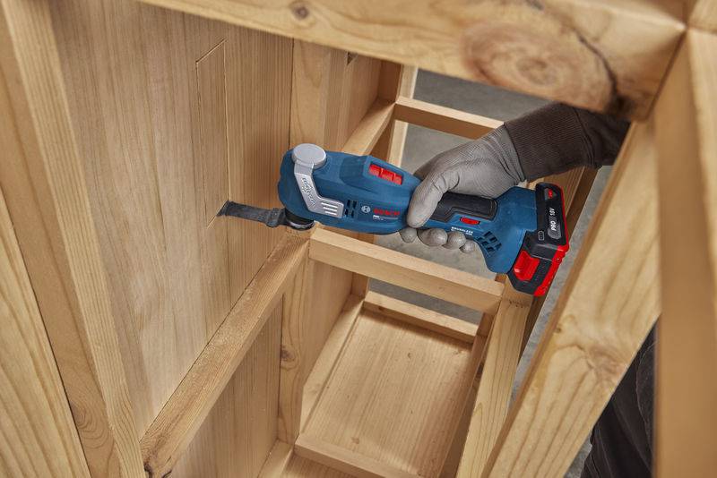 Eine Person nutzt ein Bosch-Multifunktionswerkzeug zum Schnitzen eines Holzschranks und zeigt dabei präzise Holzbearbeitungshandwerkskunst.