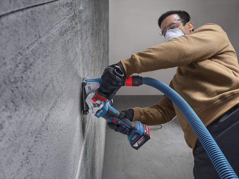 Eine Person, die Schutzausrüstung trägt, verwendet ein Elektrowerkzeug zum Schneiden einer Betonwand und demonstriert konzentrierte Anstrengung und Präzision bei einer Bauaufgabe.