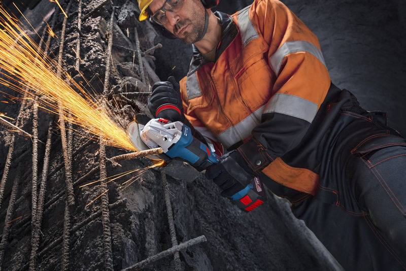 Ein Arbeiter in Schutzausrüstung schleifen Metallstangen mit einem Elektrowerkzeug und erzeugt dabei Funken auf einer Baustelle.