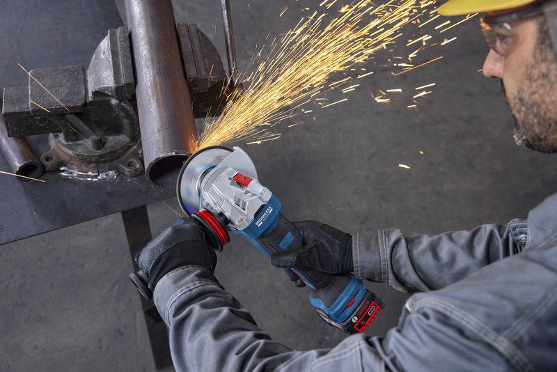 Eine Person verwendet einen Winkelschleifer zum Schneiden eines Metallrohrs, wobei Funken fliegen. Die Person trägt Schutzausrüstung, einschließlich Handschuhen und einem Helm.