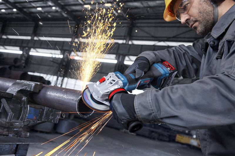 Arbeiter, der einen Winkelschleifer verwendet, um ein Metallrohr zu schneiden, wobei Funken fliegen, in einer industriellen Umgebung. Trägt Schutzausrüstung einschließlich Handschuhe und Helm.