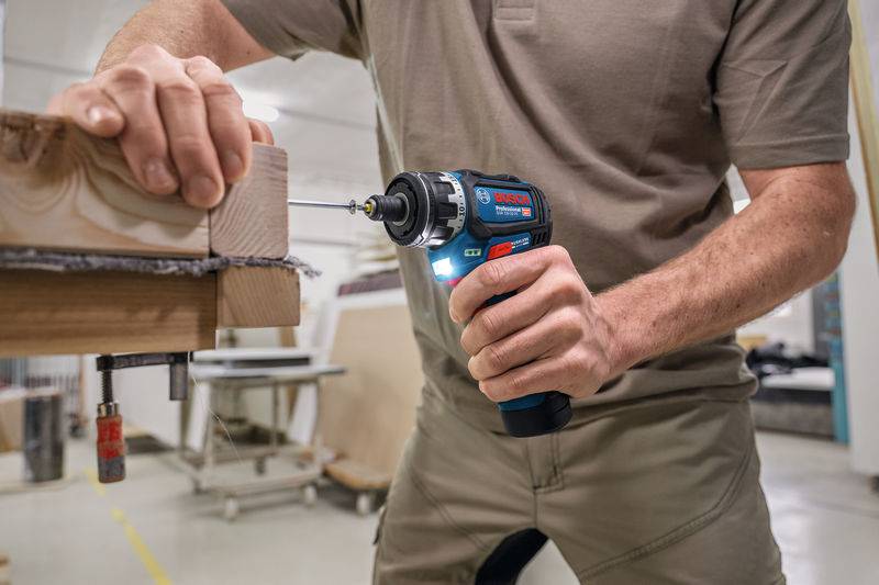 Eine Person verwendet einen Bosch Professional Elektroschrauber, um eine Schraube in verbundene Holzbretter zu treiben und demonstriert dabei Zimmermannsfertigkeiten in einer Werkstatt.