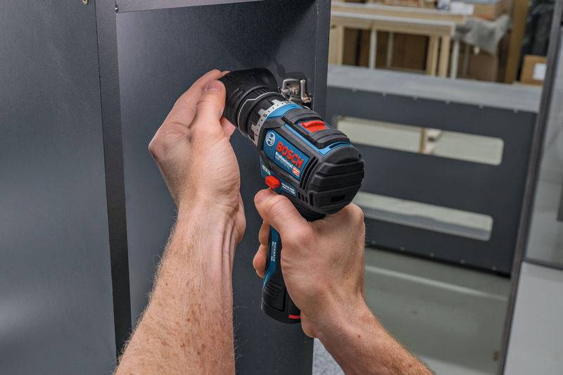 Die Hände einer Person verwenden einen Bosch-Elektroschrauber an einem grauen Metallpanel, wahrscheinlich beim Zusammenbau oder bei der Reparatur von etwas.