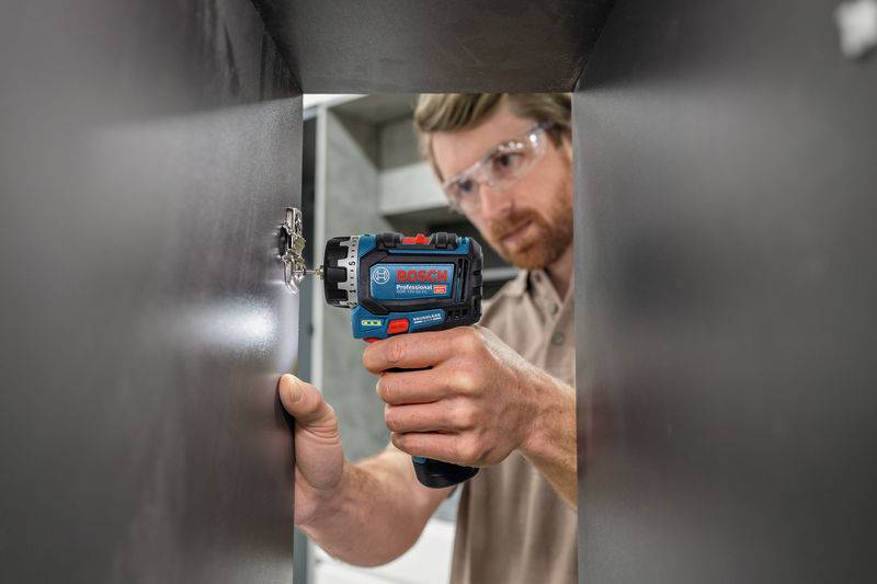 Eine Person, die eine Schutzbrille trägt, benutzt ein Bosch-Elektrowerkzeug, um ein Loch in eine dunkle Oberfläche zu bohren und konzentriert sich intensiv auf die Aufgabe.