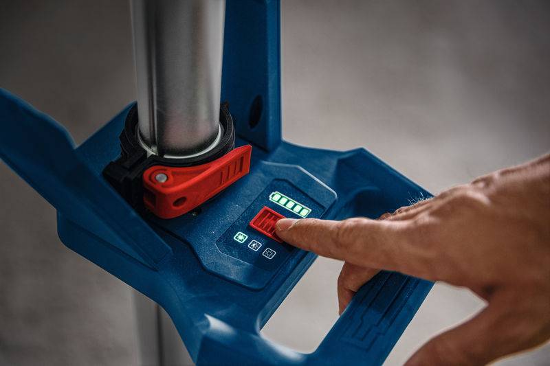 Eine Person drückt einen roten Knopf auf einem blauen Gerät mit einem kleinen digitalen Display und Symbolen, was auf ein Bedienfeld hinweist.