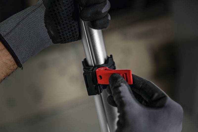 Eine Nahaufnahme von Händen, die Handschuhe tragen und einen roten Riegel um eine Metallstange sichern, was auf Montage- oder Einstellungsarbeiten hindeutet.