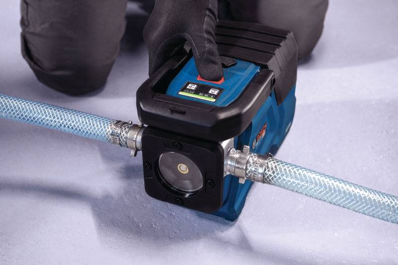 Eine Person mit Handschuhen bedient eine tragbare Wasserpumpe, die mit einem Schlauch auf einer ebenen Fläche verbunden ist.