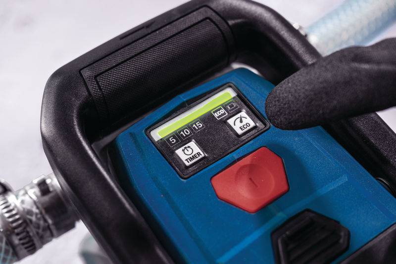 Eine behandschuhte Hand bedient ein digitales Bedienfeld mit Optionen für Timer und Eco-Modus, das an einer Maschine mit Schläuchen angebracht ist.