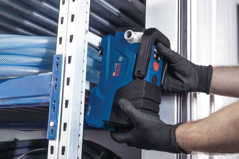 Eine Person, die Schutzhandschuhe trägt, benutzt ein blaues Elektrowerkzeug, um Metallstreben auf einer Baustelle durchzuschneiden.