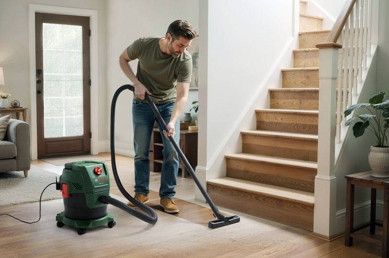 Ein Mann benutzt einen grünen Staubsauger, um Holzböden neben einer Treppe in einem gut beleuchteten Wohnzimmer zu reinigen.