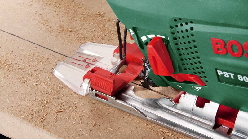 Eine Nahaufnahme einer grün und rot gefärbten Elektrostichsäge, die eine gerade Linie auf einem Holzbrett schneidet, umgeben von Holzspänen.