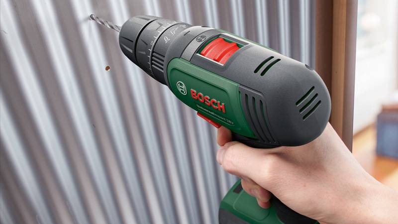 Eine Person nutzt einen Bosch-Akkubohrer, um ein Loch in ein Wellblech zu bohren, wobei der Griff und die Präzision des Bohrers hervorgehoben werden.