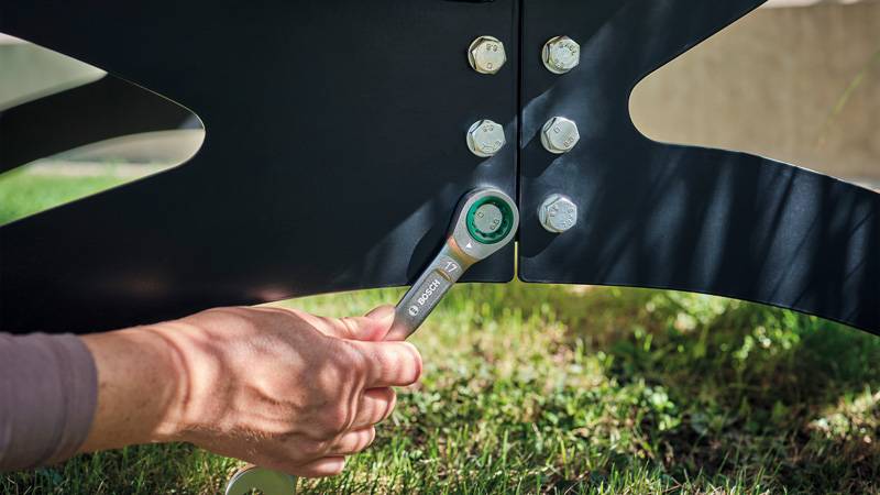 Eine Person zieht Schrauben an einer Metallkonstruktion im Freien mit einem Schraubenschlüssel an.