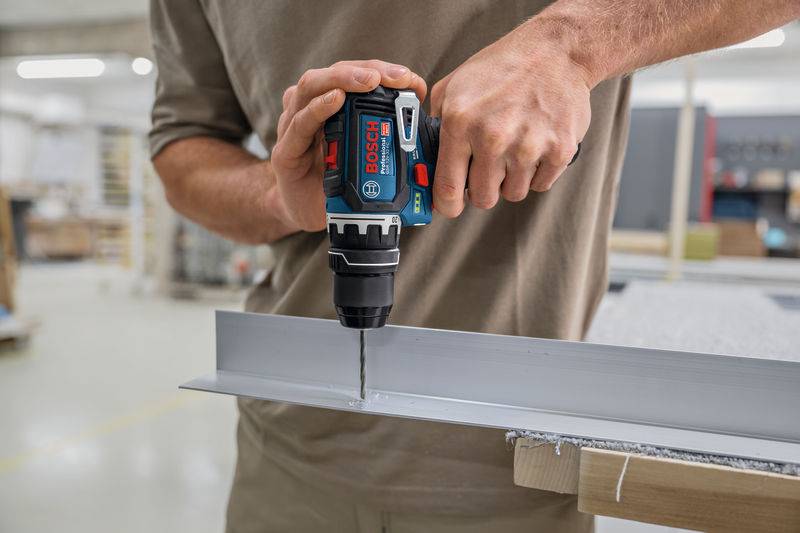 Eine Person benutzt einen Elektroschrauber, um in einer Werkstatt an einem Metallstück zu arbeiten, wobei sie sich auf Präzision und Handwerk konzentriert.