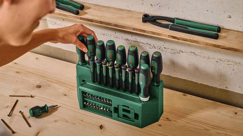 Eine Person organisiert einen Satz Schraubendreher in einem grünen Behälter auf einer hölzernen Werkbank.