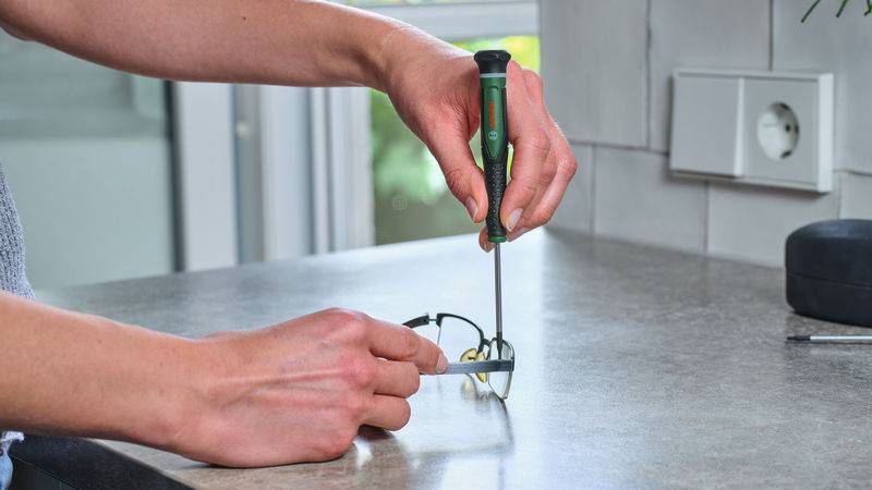 Eine Person verwendet einen Schraubendreher, um eine kleine mechanische Komponente auf einer grauen Arbeitsplatte in der Nähe einer Steckdose zusammenzubauen.