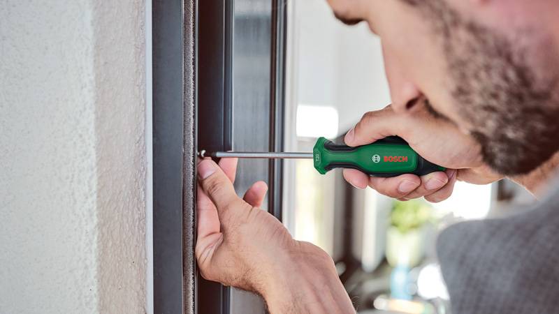 Eine Person verwendet einen Schraubendreher, um eine Schraube in einem Fensterrahmen festzuziehen, was eine Heimreparatur- oder Wartungsaufgabe demonstriert.