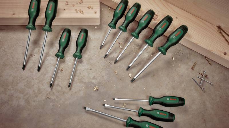 Ein Satz Schraubenzieher mit grünen Griffen in verschiedenen Größen, ausgelegt auf einer Holzoberfläche mit Schrauben und Holzspänen in der Nähe.