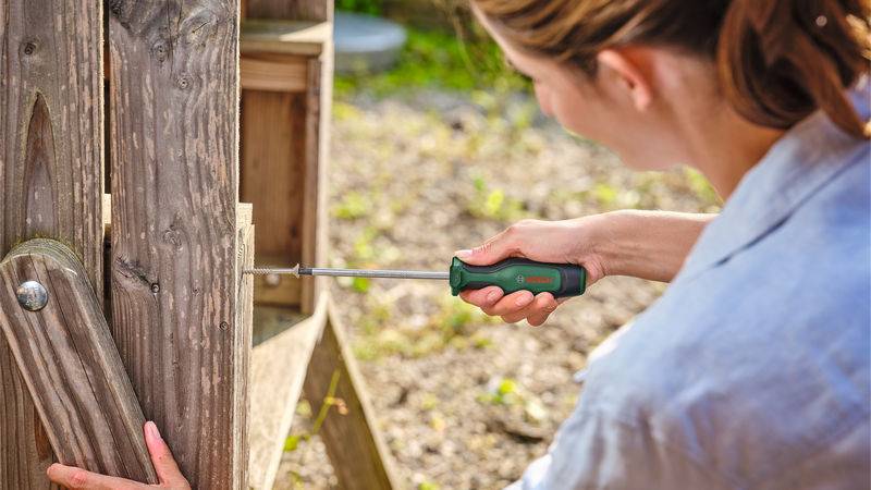 Eine Person verwendet einen Schraubendreher, um eine Schraube an einer hölzernen Außenstruktur festzuziehen und konzentriert sich auf Wartungs- oder Montagearbeiten.