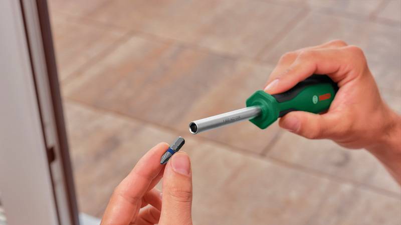 Eine Person hält ein kleines Torx-Schraubendreherbit und ist dabei, es in einen grünen Schraubendrehergriff mit einer silbernen Metallachse einzuführen.