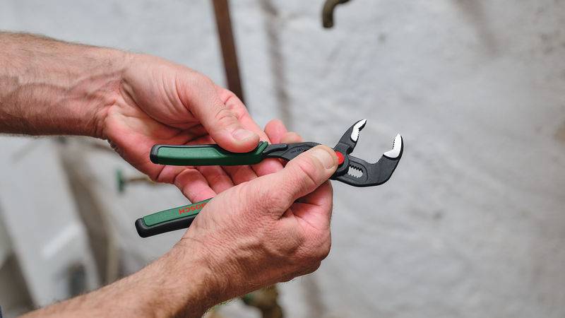 Eine Person verwendet grüne Rohrzangen, um ein Rohr einzustellen, möglicherweise bei einer Sanitäraufgabe.