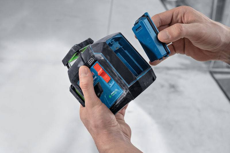 Zwei Hände, die ein Lasernivelliergerät halten, zeigen das Batteriefach und demonstrieren das Einsetzen oder Entfernen der Batterie für den Betrieb.