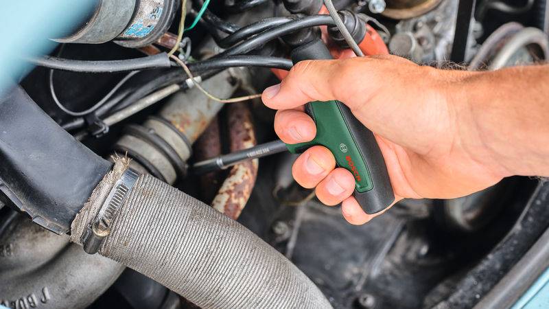 Eine Hand, die einen Schraubendreher verwendet, um Automotorkomponenten einzustellen, wobei DIY-Autowartung hervorgehoben wird.