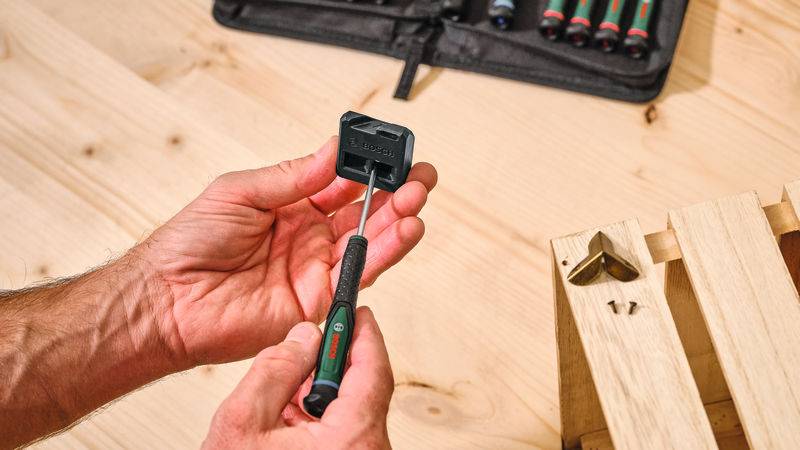 Eine Person, die einen Schraubenzieher hält, montiert Möbel auf einer Holzoberfläche, mit einem Werkzeugkasten im Hintergrund sichtbar.