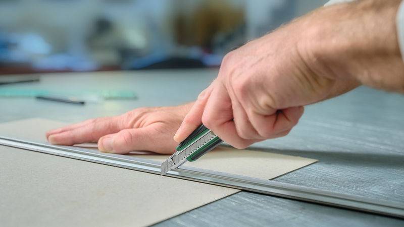 Eine Person benutzt ein Universalmesser, um Papier mit einem Stahllineal auf einem Tisch zu schneiden.