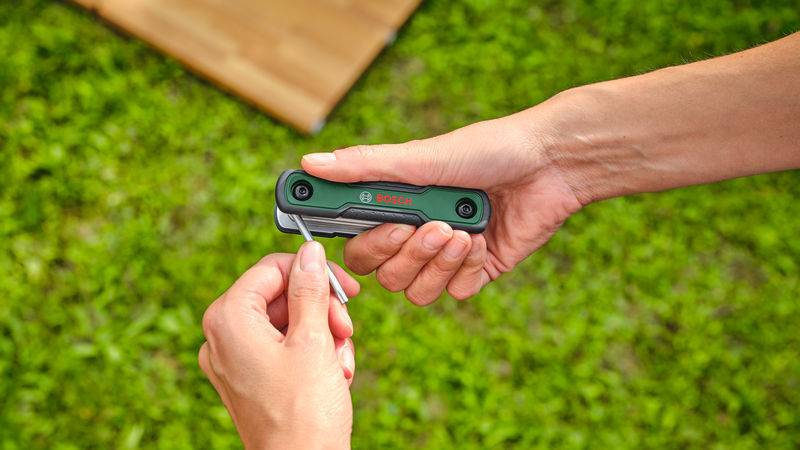 Eine Person öffnet ein schwarzes Taschenmesser mit dem Bosch-Logo und zeigt es vor einem Grashintergrund.