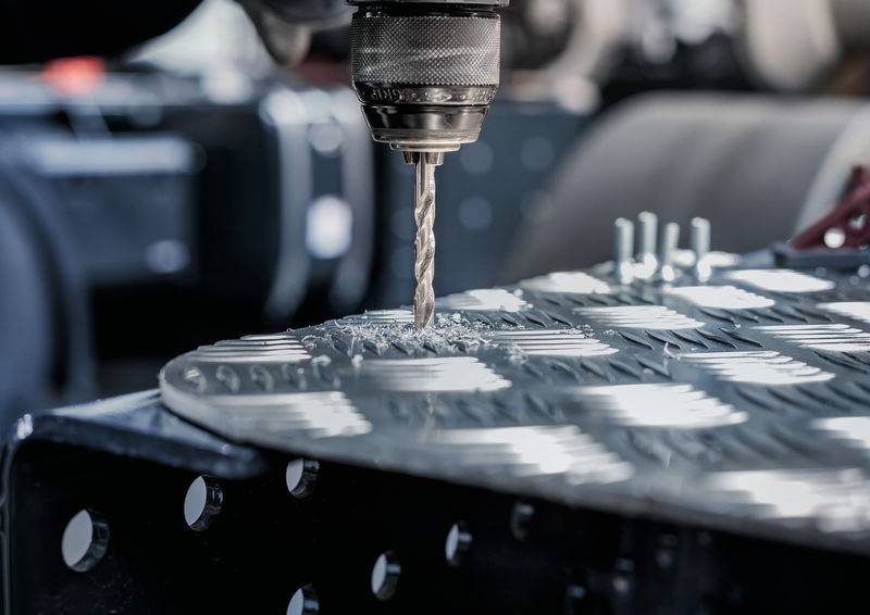 Ein kreisförmiger Metallbohrer erstellt Löcher in einem strukturierten Metallblech, wobei Metallspäne um den Bohrmeißel sichtbar sind.