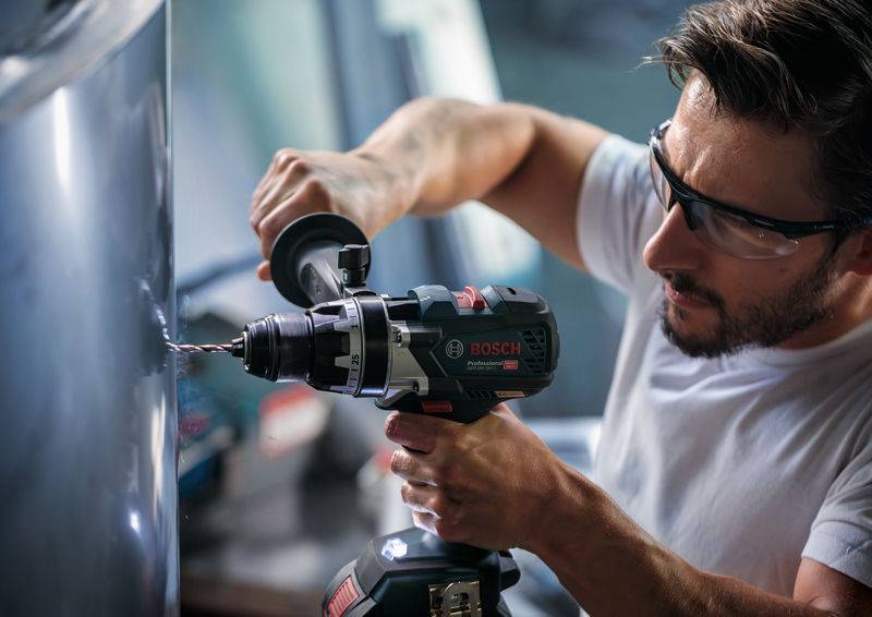 Eine Person, die eine Schutzbrille trägt, benutzt einen Bosch-Elektroschrauber, um an einer Metalloberfläche zu arbeiten.