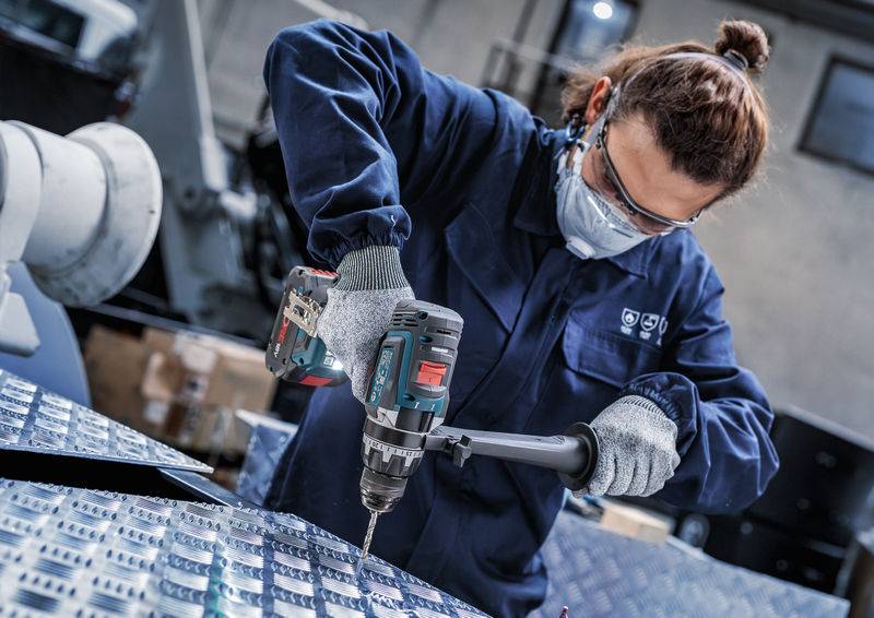Eine Person in Schutzausrüstung bedient einen Akku-Bohrschrauber auf einem Metallblech in einer Werkstatt und unterstreicht damit Konzentration und Präzision in der Industriearbeit.