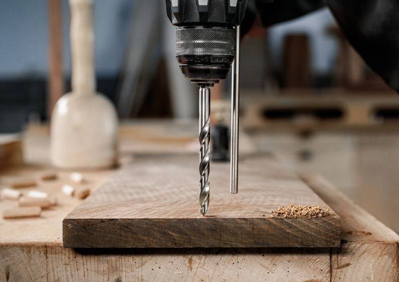 Eine Nahaufnahme einer Elektrobohrmaschine, die in ein Holzbrett bohrt, mit Holzspänen, die überall verstreut sind, in einer Werkstattumgebung.