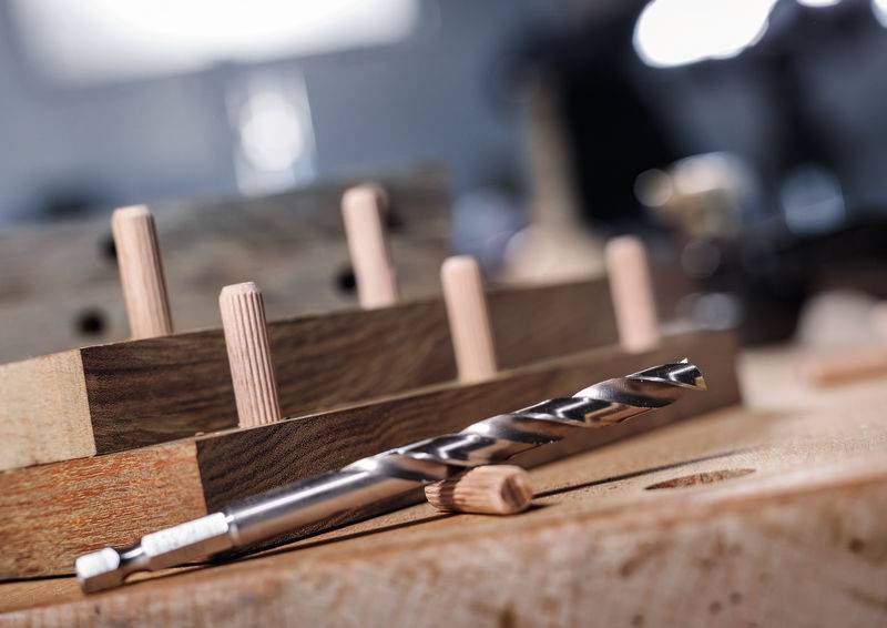 Eine Nahaufnahme einer Holzwerkbank mit Dübeln und einem Bohrer, die ein laufendes Holzbearbeitungsprojekt andeuten.