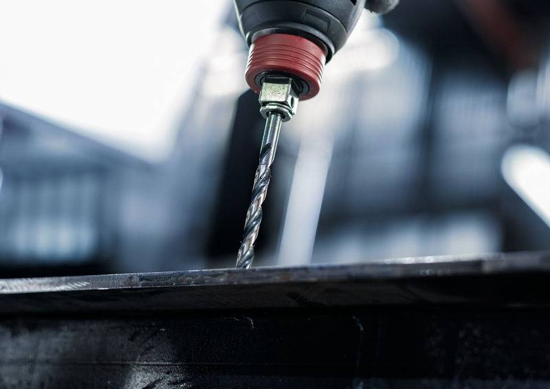 Ein Bohrereindringend in eine Metalloberfläche in einer Werkstattumgebung, wobei die Bohrmaßnahme gezeigt wird und der Fokus auf der Präzision des Werkzeugs liegt.