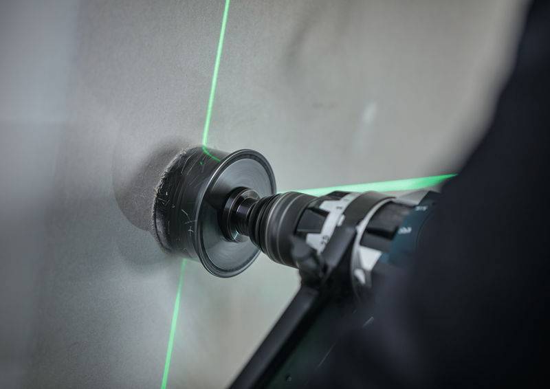 Ein Elektrobohrer mit einer Lochsäge erzeugt einen kreisförmigen Schnitt in einer Wand. Eine grüne Laserlinie unterstützt die Ausrichtung.