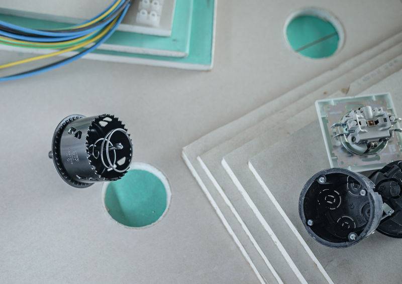 Elektrische Komponenten auf einer Betonplatte mit gebohrten Löchern, die Verdrahtungsvorbereitungen für Installationen zeigen.