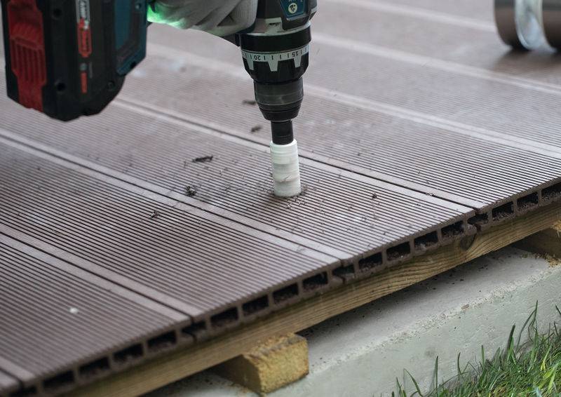 Ein Elektrowerkzeug bohrt ein Loch in ein braunes, gerilltes Holzdeckenbrett, wobei Konstruktions- oder Heimwerkerarbeiten gezeigt werden.